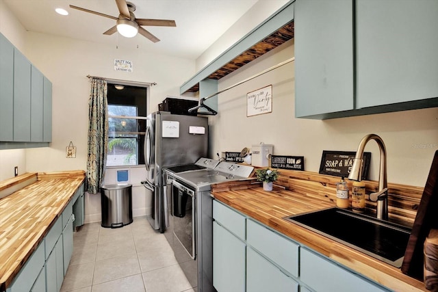 kitchen featuring wooden counters, sink, light tile patterned floors, and washing machine and clothes dryer