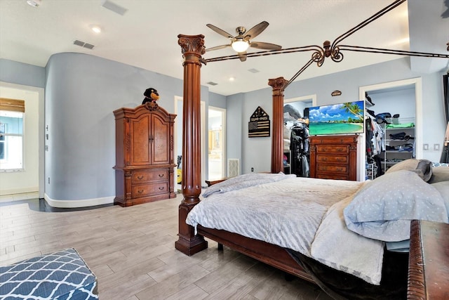 bedroom featuring a walk in closet, light hardwood / wood-style floors, a closet, and ornate columns