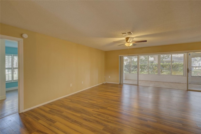 unfurnished room with ceiling fan, a wealth of natural light, wood-type flooring, and a textured ceiling