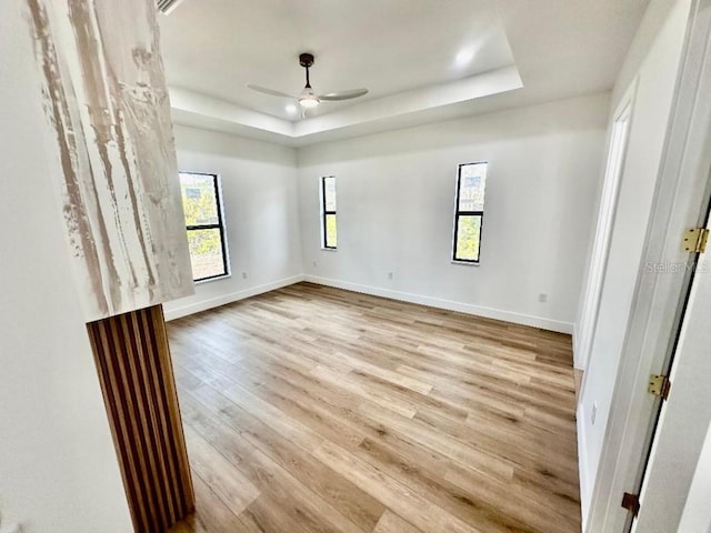 unfurnished room with ceiling fan, a raised ceiling, and light wood-type flooring