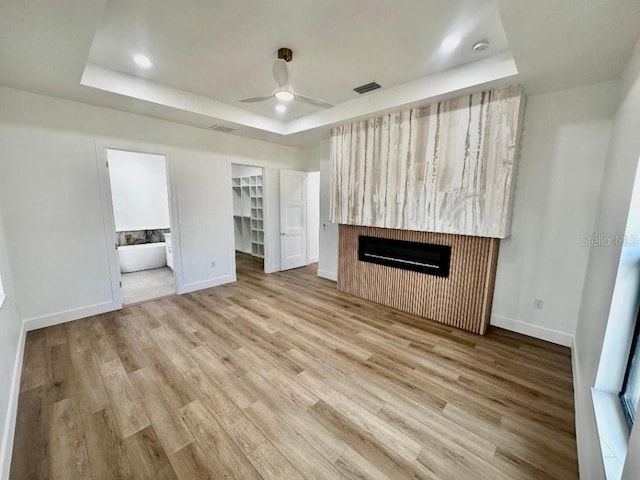 unfurnished living room with ceiling fan, a raised ceiling, and light wood-type flooring