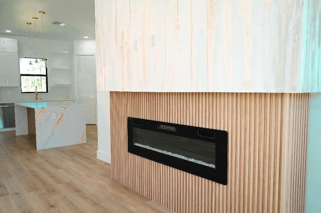 interior details featuring visible vents, stainless steel dishwasher, a glass covered fireplace, a sink, and wood finished floors