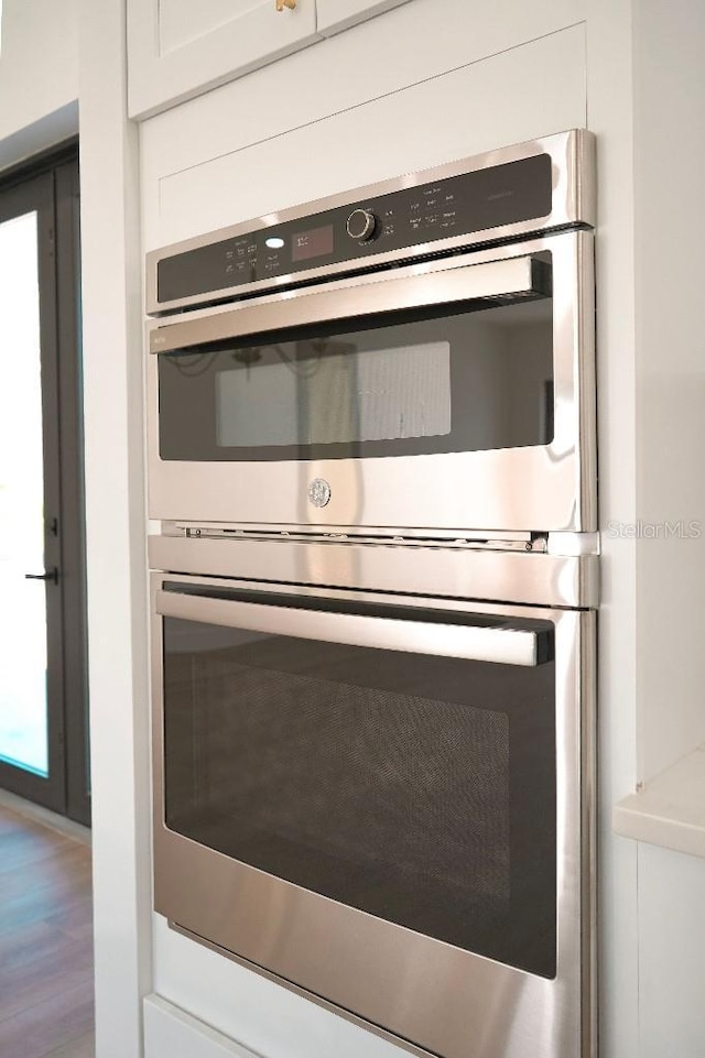 room details with double oven, white cabinetry, and wood finished floors