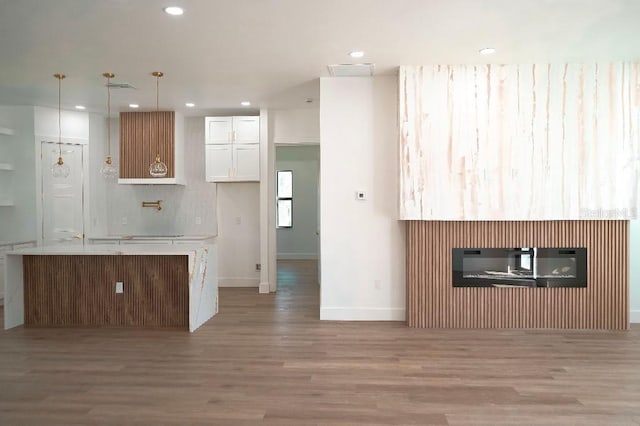 kitchen featuring light wood-style floors, white cabinets, light countertops, a glass covered fireplace, and decorative light fixtures