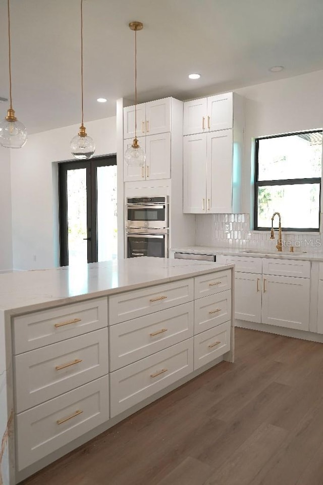 kitchen with dark wood finished floors, white cabinets, a sink, pendant lighting, and backsplash