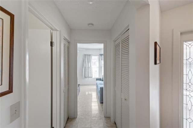 hall with a textured ceiling and light tile patterned floors