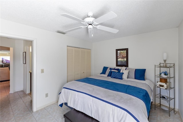 bedroom with light tile patterned flooring, ceiling fan, a closet, and a textured ceiling