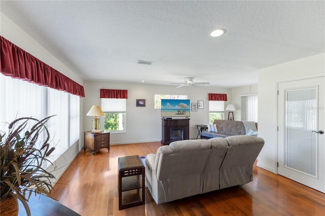 living room featuring wood-type flooring, ceiling fan, and a textured ceiling