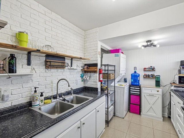 kitchen featuring light tile patterned flooring, stacked washer / drying machine, sink, white cabinetry, and brick wall