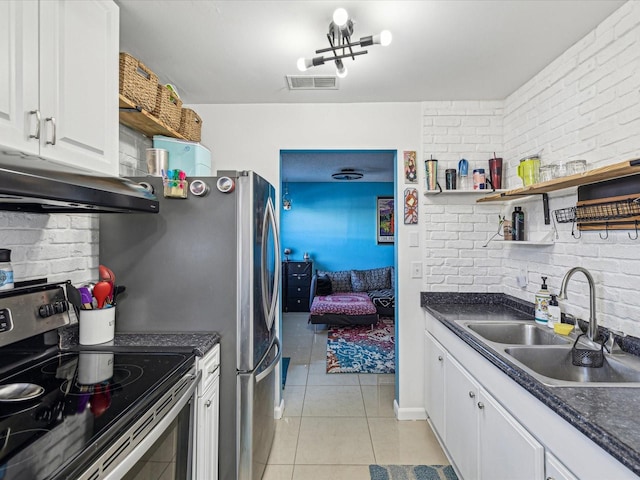 kitchen with sink, light tile patterned floors, appliances with stainless steel finishes, white cabinets, and brick wall