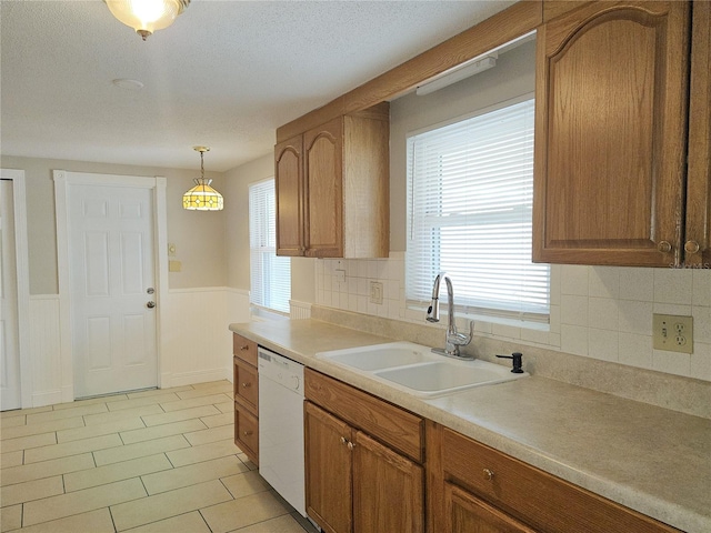 kitchen featuring a healthy amount of sunlight, white dishwasher, sink, and hanging light fixtures