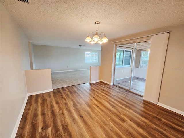 spare room featuring an inviting chandelier, wood-type flooring, and a textured ceiling