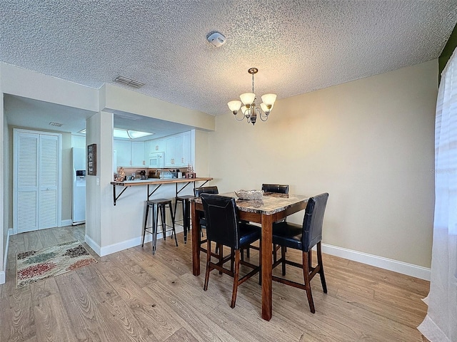 dining room with an inviting chandelier, light hardwood / wood-style flooring, and a textured ceiling