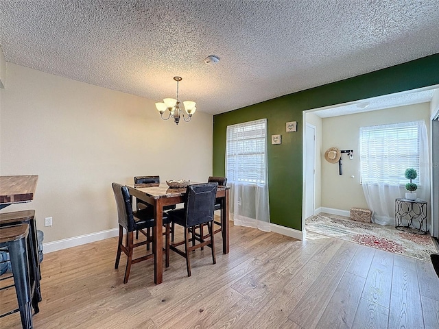 dining space featuring a notable chandelier, a textured ceiling, and light hardwood / wood-style flooring