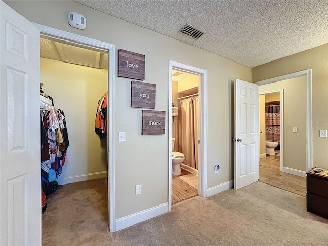 bedroom with a spacious closet, light carpet, a textured ceiling, ensuite bath, and a closet