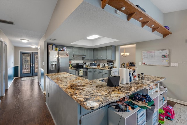 kitchen featuring an inviting chandelier, dark hardwood / wood-style floors, gray cabinets, stainless steel appliances, and decorative backsplash