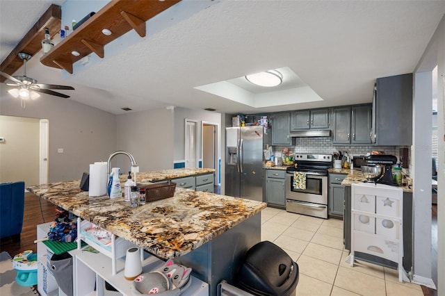 kitchen featuring gray cabinets, appliances with stainless steel finishes, light tile patterned flooring, decorative backsplash, and a raised ceiling