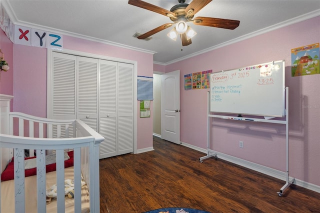 bedroom with dark wood-type flooring, crown molding, a closet, a nursery area, and ceiling fan