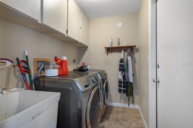 clothes washing area with sink, washing machine and dryer, cabinets, a textured ceiling, and light tile patterned flooring