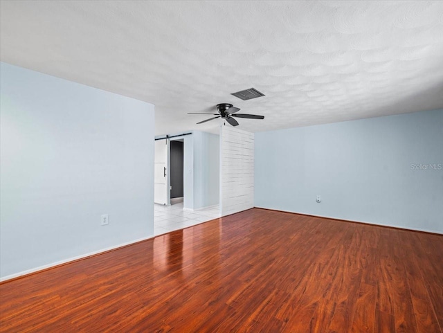 unfurnished room with ceiling fan, a barn door, a textured ceiling, and light wood-type flooring