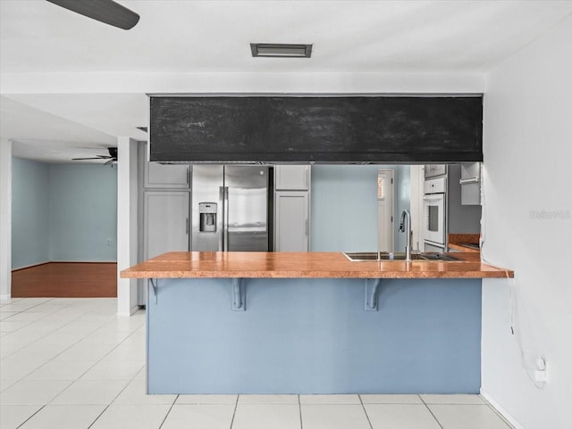 kitchen featuring stainless steel refrigerator with ice dispenser, a breakfast bar, sink, kitchen peninsula, and ceiling fan