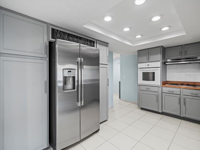 kitchen with stainless steel appliances, a tray ceiling, gray cabinets, and backsplash