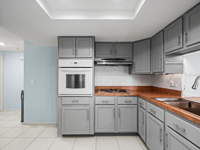 kitchen featuring a tray ceiling, gray cabinets, sink, and white oven