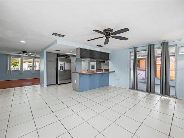 kitchen featuring stainless steel refrigerator with ice dispenser, a breakfast bar, kitchen peninsula, ceiling fan, and white oven