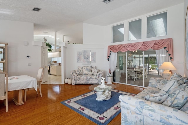 living room featuring wood-type flooring, high vaulted ceiling, and a textured ceiling