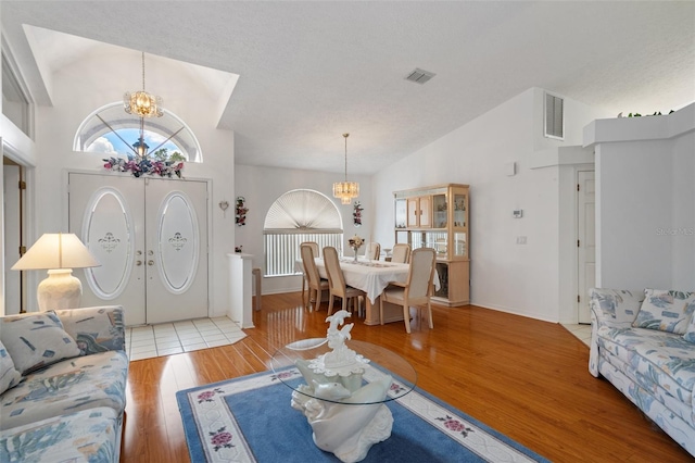 living room with an inviting chandelier, hardwood / wood-style floors, vaulted ceiling, and a textured ceiling