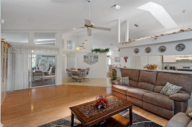 living room featuring ceiling fan, high vaulted ceiling, light hardwood / wood-style floors, and a skylight