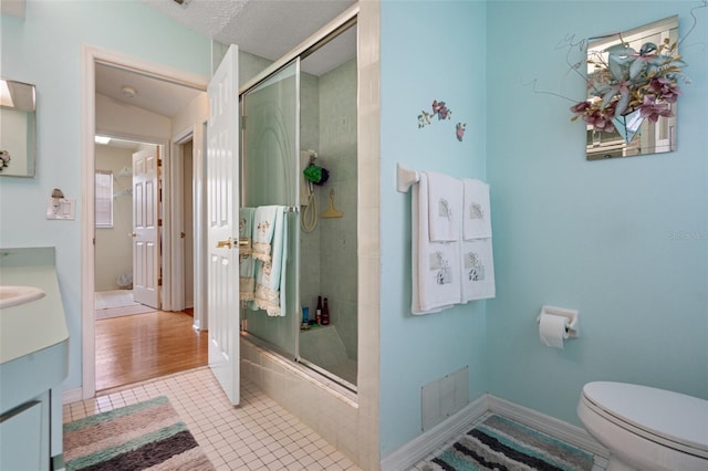 bathroom featuring vanity, toilet, a shower with door, tile patterned floors, and a textured ceiling