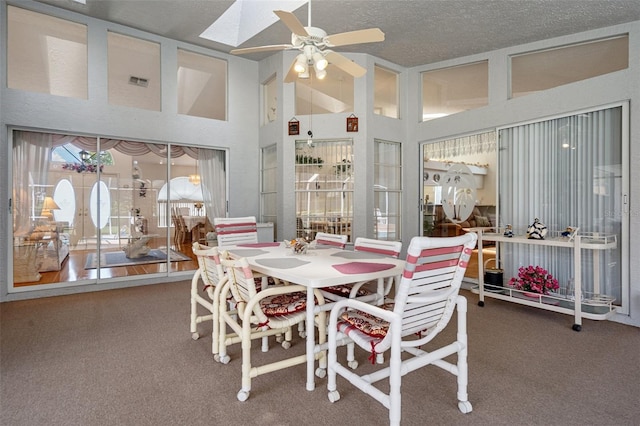 carpeted dining space with high vaulted ceiling, a skylight, ceiling fan, a textured ceiling, and french doors