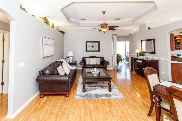 living room with crown molding, a tray ceiling, and light wood-type flooring