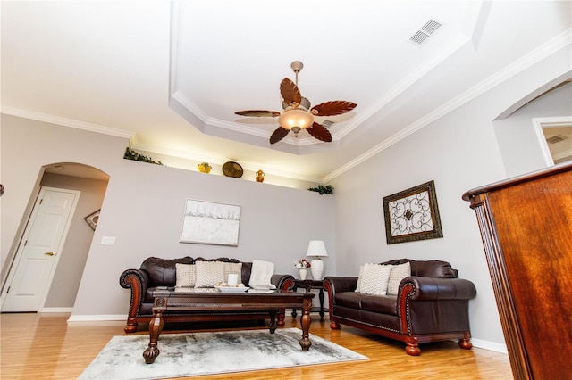 living room with ceiling fan, ornamental molding, a raised ceiling, and light hardwood / wood-style floors