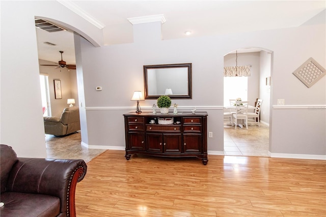 corridor with crown molding, light hardwood / wood-style floors, and a notable chandelier