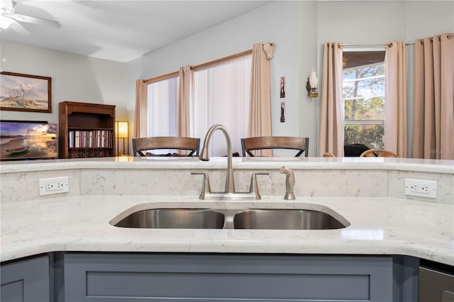 kitchen with gray cabinetry, sink, light stone counters, and ceiling fan