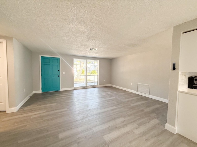 unfurnished living room with a textured ceiling and light hardwood / wood-style floors