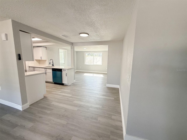 kitchen featuring white cabinetry, sink, stainless steel dishwasher, light hardwood / wood-style floors, and a textured ceiling