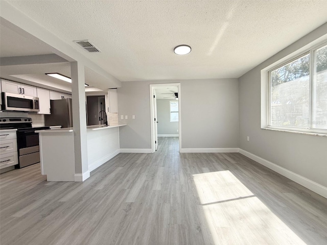 kitchen featuring tasteful backsplash, light wood-type flooring, white cabinets, and appliances with stainless steel finishes