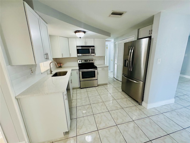 kitchen featuring appliances with stainless steel finishes, white cabinetry, sink, decorative backsplash, and light tile patterned floors