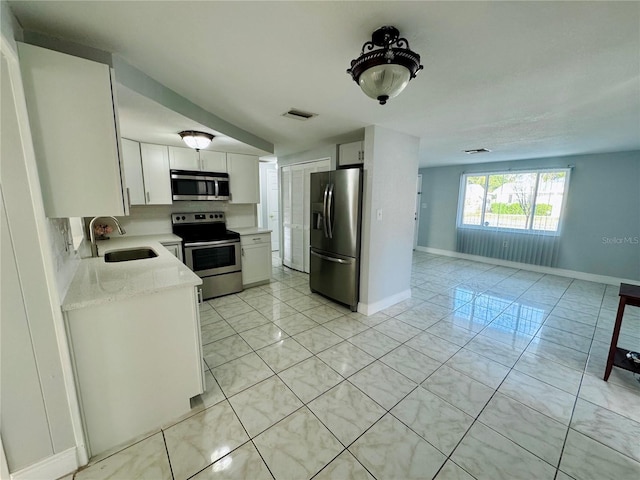 kitchen with white cabinetry, appliances with stainless steel finishes, light stone countertops, and sink