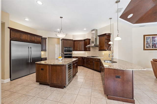 kitchen featuring dark brown cabinetry, sink, kitchen peninsula, built in fridge, and wall chimney range hood