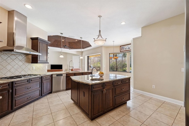 kitchen with appliances with stainless steel finishes, decorative light fixtures, sink, a center island with sink, and wall chimney exhaust hood