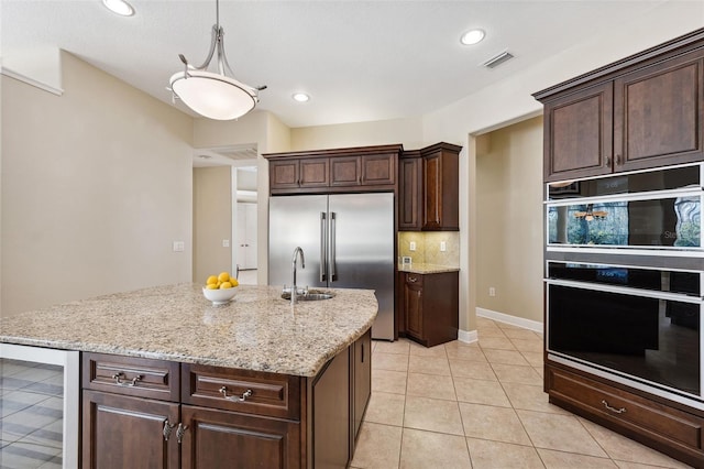 kitchen featuring a kitchen island with sink, dark brown cabinets, black double oven, decorative light fixtures, and beverage cooler