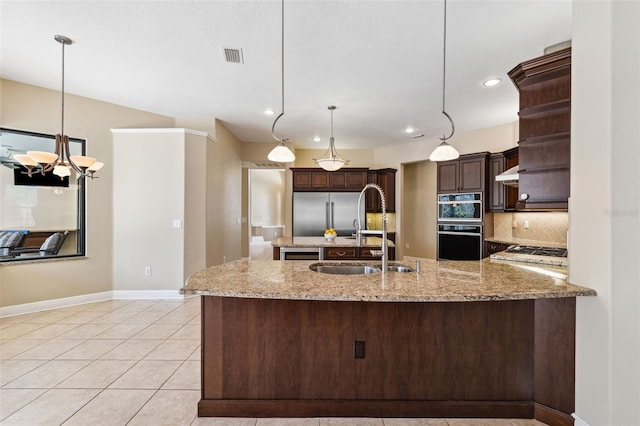 kitchen featuring sink, dark brown cabinetry, tasteful backsplash, light stone counters, and decorative light fixtures