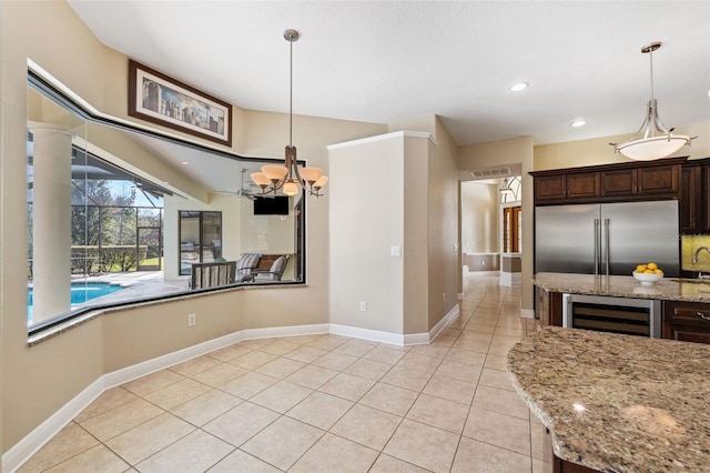 kitchen featuring wine cooler, dark brown cabinetry, light tile patterned floors, pendant lighting, and light stone countertops