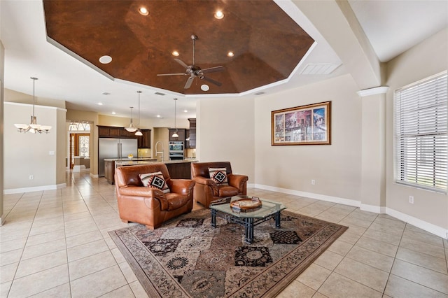 living room featuring ceiling fan with notable chandelier, sink, light tile patterned floors, and a tray ceiling