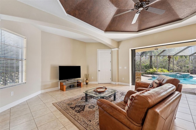 living room with a raised ceiling, light tile patterned floors, a textured ceiling, and ceiling fan