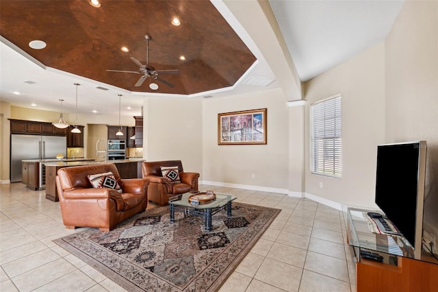 tiled living room with ceiling fan and a tray ceiling